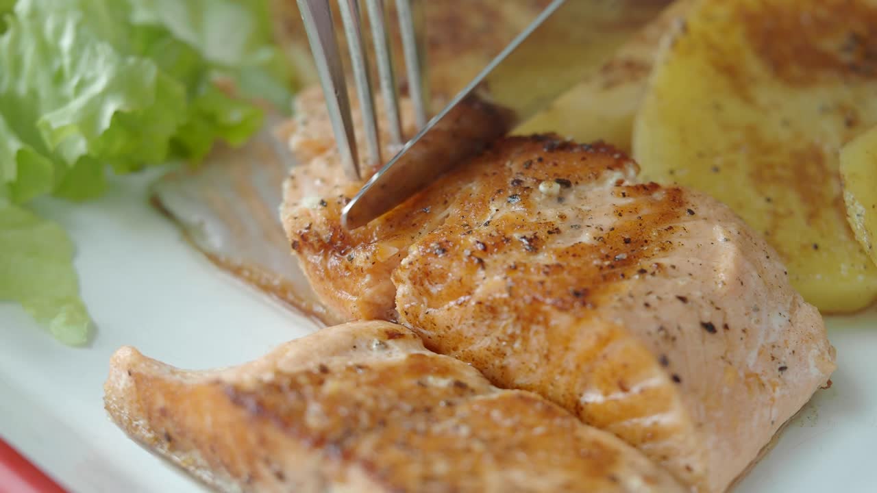 Primer plano de un filete de salmón cocido siendo cortado en un plato