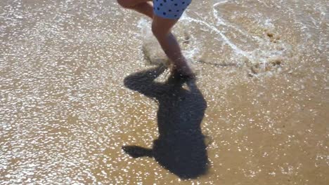 Close-up-of-a-three-year-old-boy's-feet-running-along-the-beach-and-splashing-in-the-waves-in-slow-motion