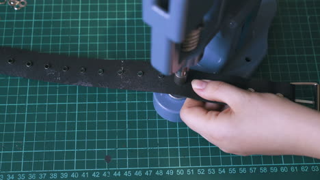 skilled worker fixes silver eyelets on fashionable belt