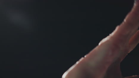 Side view of manicured hand covered in melting snow illuminated by soft night light against dark background, revealing textured skin details and subtle warmth in contrast with icy particles