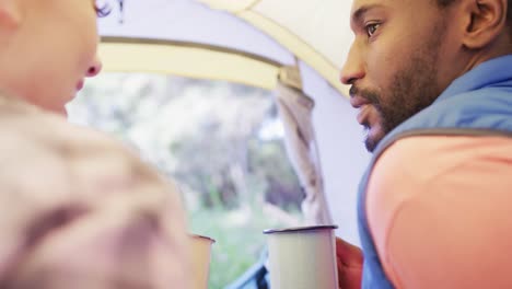 Happy-diverse-couple-drinking-tea-and-sitting-in-tent,-slow-motion