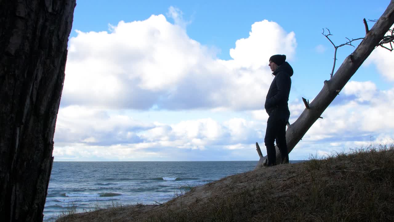 북유럽 해변 숲을 탐험하는 백인 남성의 뒷모습, 발트해 해변 근처의 해안 소나무 숲에 홀로 서 있는 남자, 구름과 함께 화창한 날, 건강한 활동 개념, 먼 와이드 샷