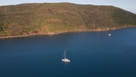 velero a la deriva en la superficie de la isla hook en el área de whitsunday con una entrada verde y exuberante en el fondo