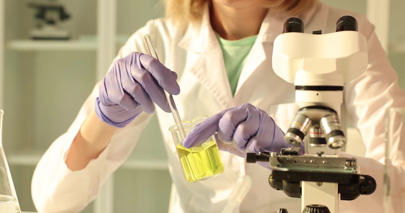 Female scientist stirs yellow solution in beaker for lab test