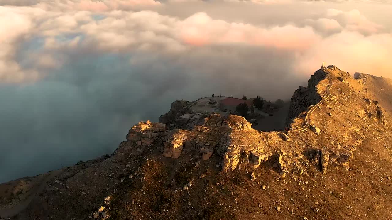 Cinematic aerial views of a historic church emerging from fog-shrouded mountains, bathed in warm sunset light