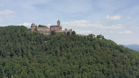 Toma-Aérea-Cuesta-Arriba-Que-Muestra-Un-Castillo-Medieval-Renovado-En-La-Región-De-Alsacia-De-Francia