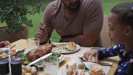 happy biracial father and daughter eating meal at dinner table in garden, slow motion