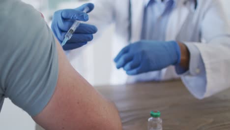 mixed race male doctor wearing face mask giving vaccine to male patient at home