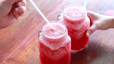 hands prepare watermelon juice in glass jars on a wooden table under natural light, capturing a refreshing moment