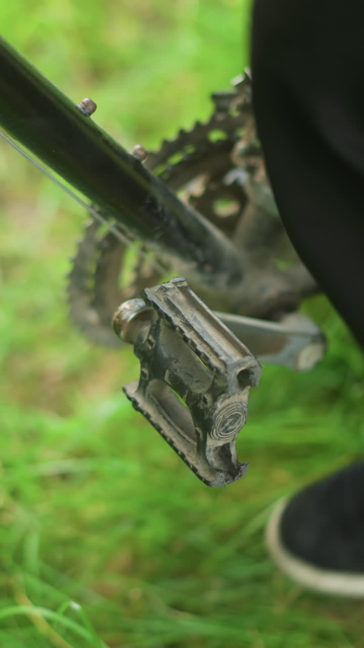 Close-up of someone wearing grey sneakers tapping and rotating bicycle pedal in grassy field, placing foot on the pedal, adjust the sneaker before stepping down onto the grassy ground