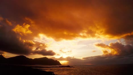 Aerial-view,-Tilting-down-from-the-golden-sunset-lit-clouds-to-the-beautiful-sea-of-flakstad,-Lofoten-Islands,-Norway