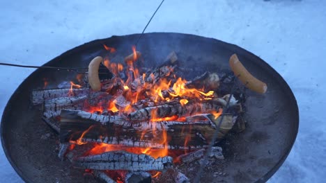 roasting sausages on sticks over a warm, roaring fire, cozy winter outdoor cookout