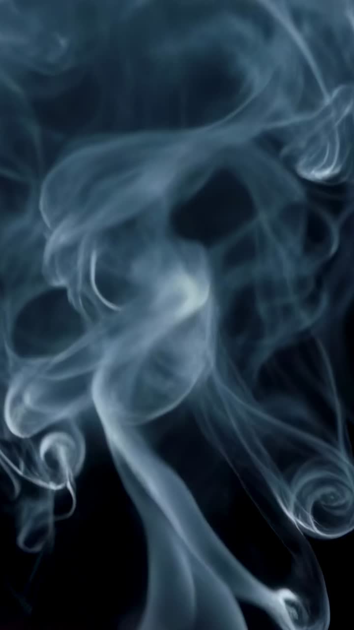 Video verticale: colonna di fumo blu che sale sotto l'inquadratura, con anelli e nastri arricciati illuminati in studio