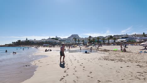 sunny day at a bustling beach with many vacationers and coastal buildings