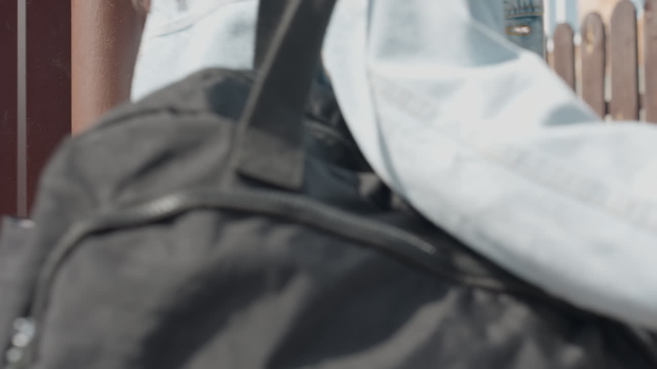 Rear view of lady wearing white crop top and jeans with smartphone in back pocket opening brown metal door as friend follows closely behind during sunny day, casual urban outdoor movement