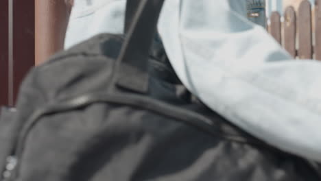 rear view of lady wearing white crop top and jeans with smartphone in back pocket opening brown metal door as friend follows closely behind during sunny day, casual urban outdoor movement
