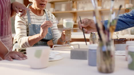 Happy-diverse-group-of-potters-glazing-clay-jugs-and-discussing-in-pottery-studio