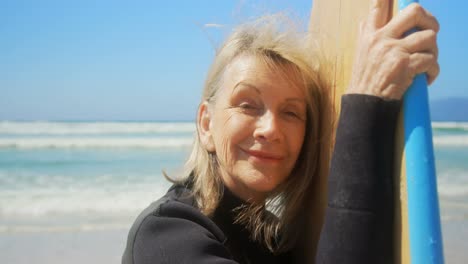 Front-view-of-active-senior-Caucasian-female-surfer-standing-with-surfboard-on-the-beach-4k