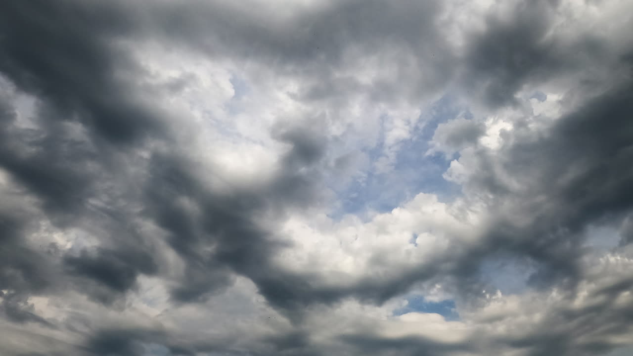 Light stratus clouds quickly transform into heavy grey cloudscape. Low angle view on the clouds transforming in atmosphere. Timelapse.
