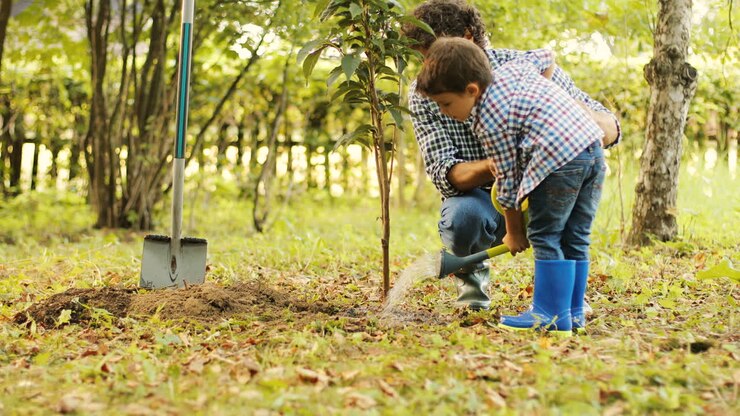 Portrait of a boy and his dad watering a tree. Dad helps his son. Blurred background