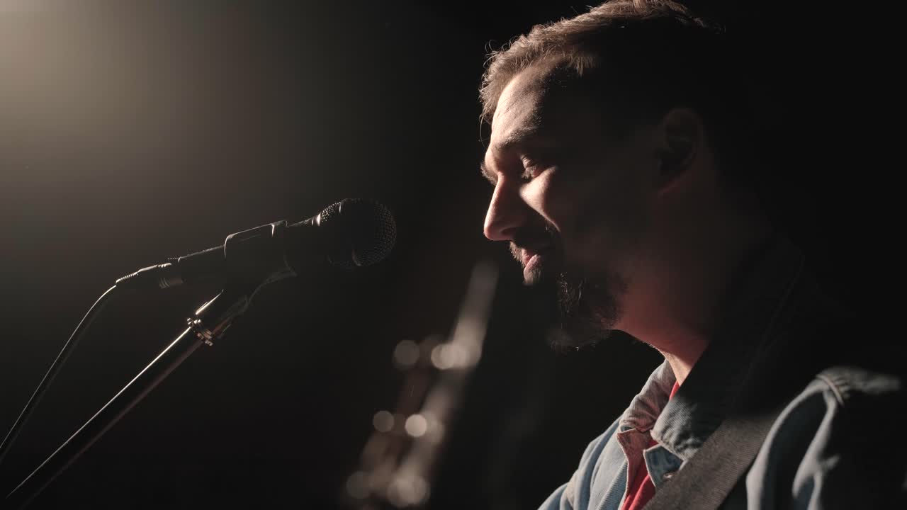 un músico está tocando la guitarra en un gran escenario con miembros de la audiencia sosteniendo linternas en el fondo. el auditorio está lleno de hermosas luces parpadeantes.