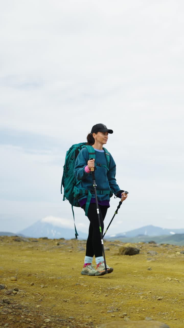 Donna che fa escursioni con zaino e bastoncini da trekking in un paesaggio montano