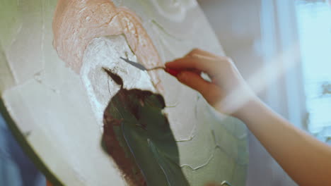 hand of artist applying paint to canvas with palette knife in creative studio