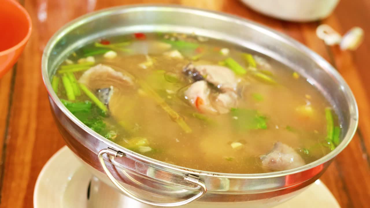 una persona sirve sopa picante de costillas de cerdo tailandesa de una olla, destacando ingredientes vibrantes y caldo rico en un entorno cálido