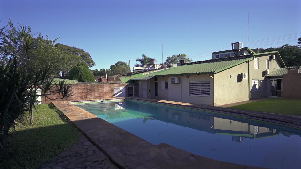 Sunlit house backyard with swimming pool at suburban environment under blue sky.
