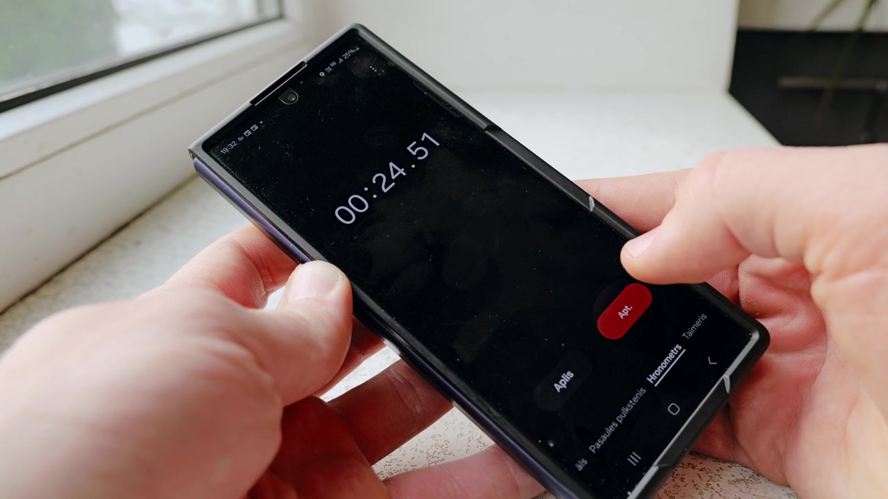 Primo piano di mani maschili che usano il timer dello smartphone vicino a una finestra all'interno