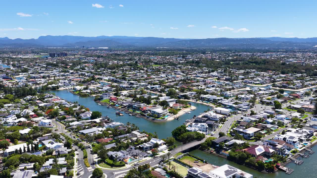 Drone glides over waterfront houses, canals, and cityscape on a clear, sunny day