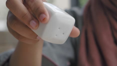 a close-up of a woman's hand sprinkling salt from a white shaker onto food