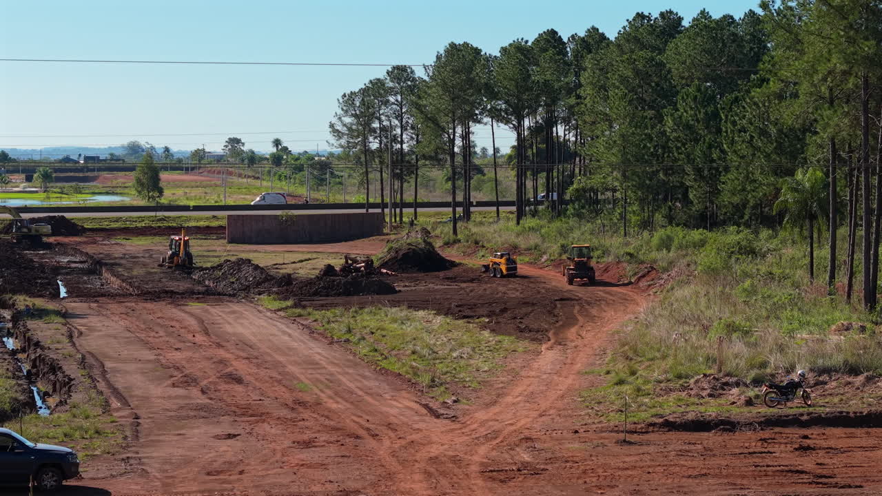 Ground-skimming drone glides over rural construction, framing bulldozers, bobcats, and pine rows against a sunlit highway. Ideal for heavy equipment or infrastructure reels.