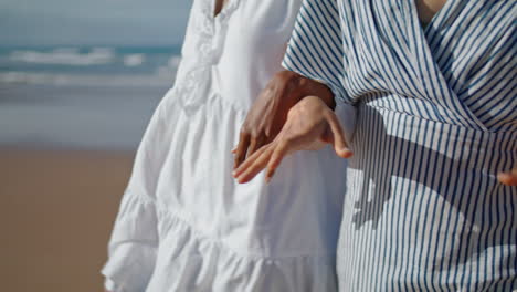 closeup couple hands walking ocean coast in sunlight. girlfriends enjoying date