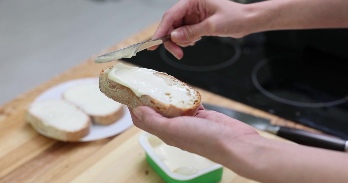 Female spreads cream cheese on slice of bread with knife