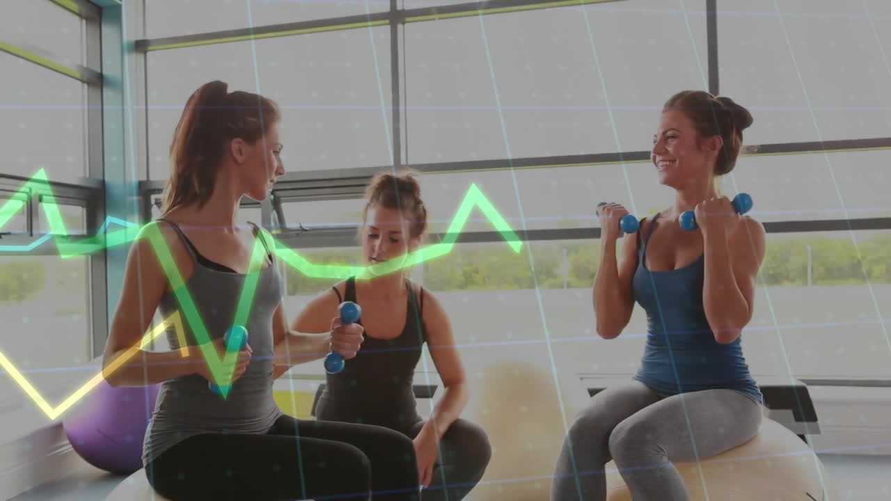Three women exercising on stability balls in gym, lifting blue dumbbells with floating health chart