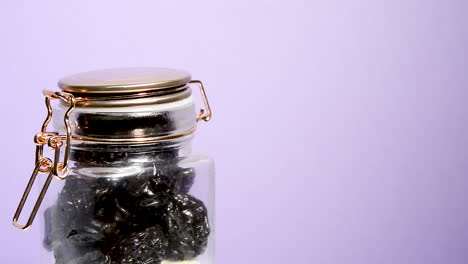 An-airtight-mason-jar-rotating-with-dried-plums-on-a-neon-lilac-background