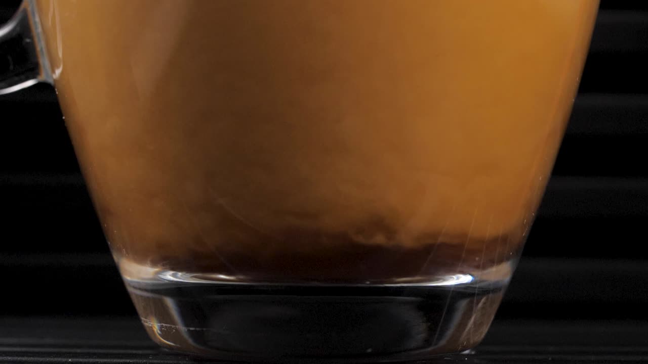 The bottom part of a transparent glass cup, filled with coffee and cream