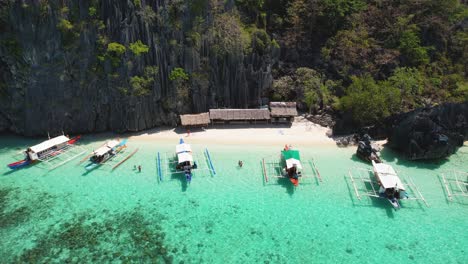 4k drone video looking at boats docked up and people swimming on banal beach while on day trips from coron in palawan, philippines