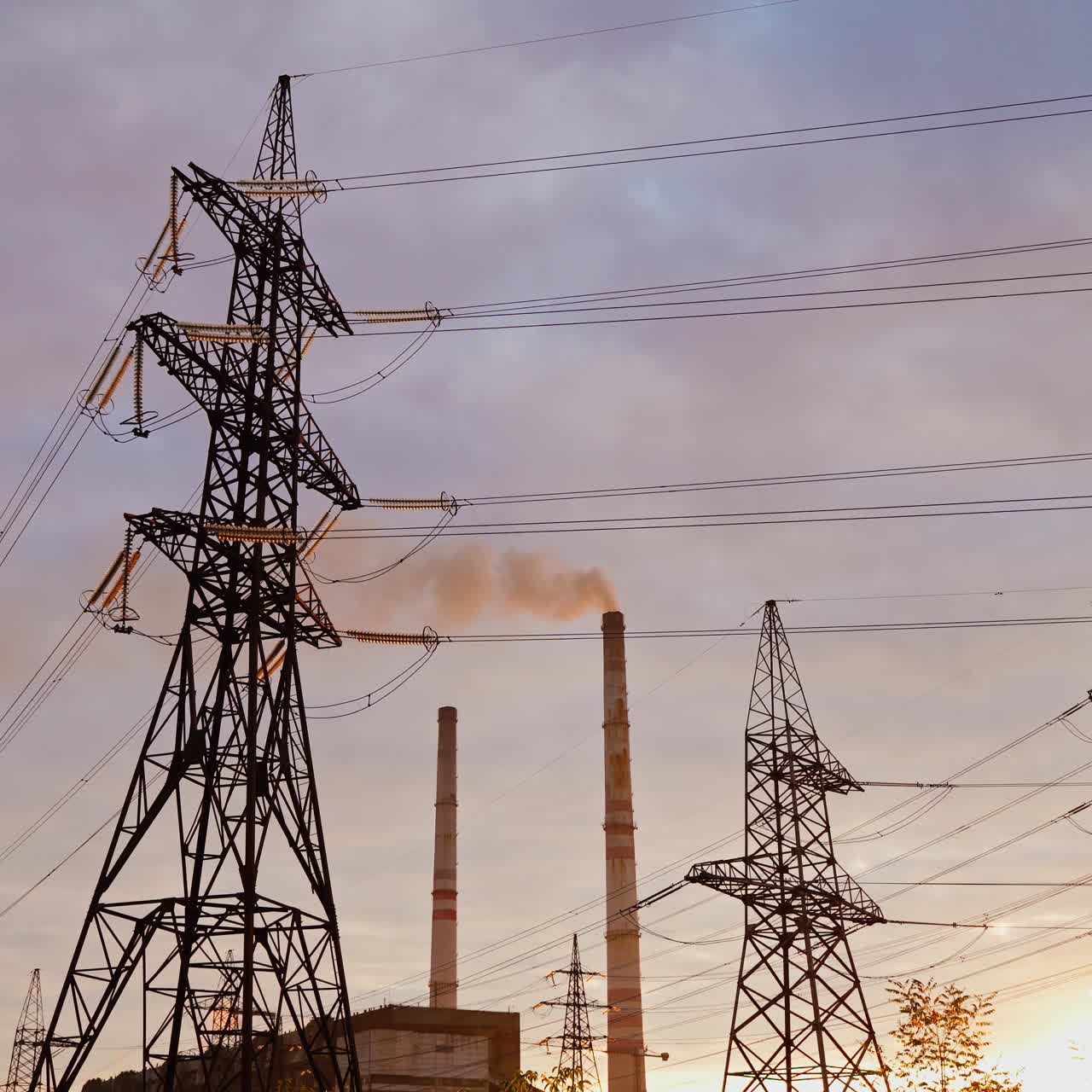 Electricity pylons against orange and yellow sunset. Selective focus. Video from the side