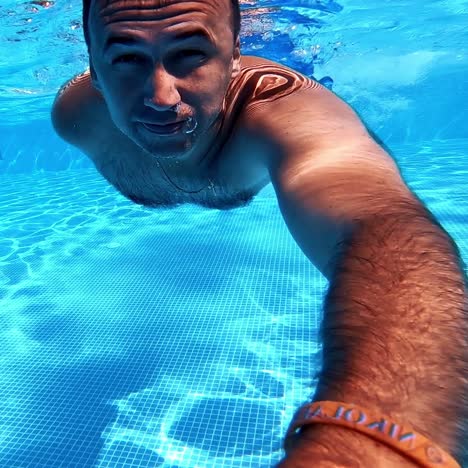 man underwater in the pool. healthy man swimming inside the blue clear water of the swimming pool and looking to camera. summer vacation.