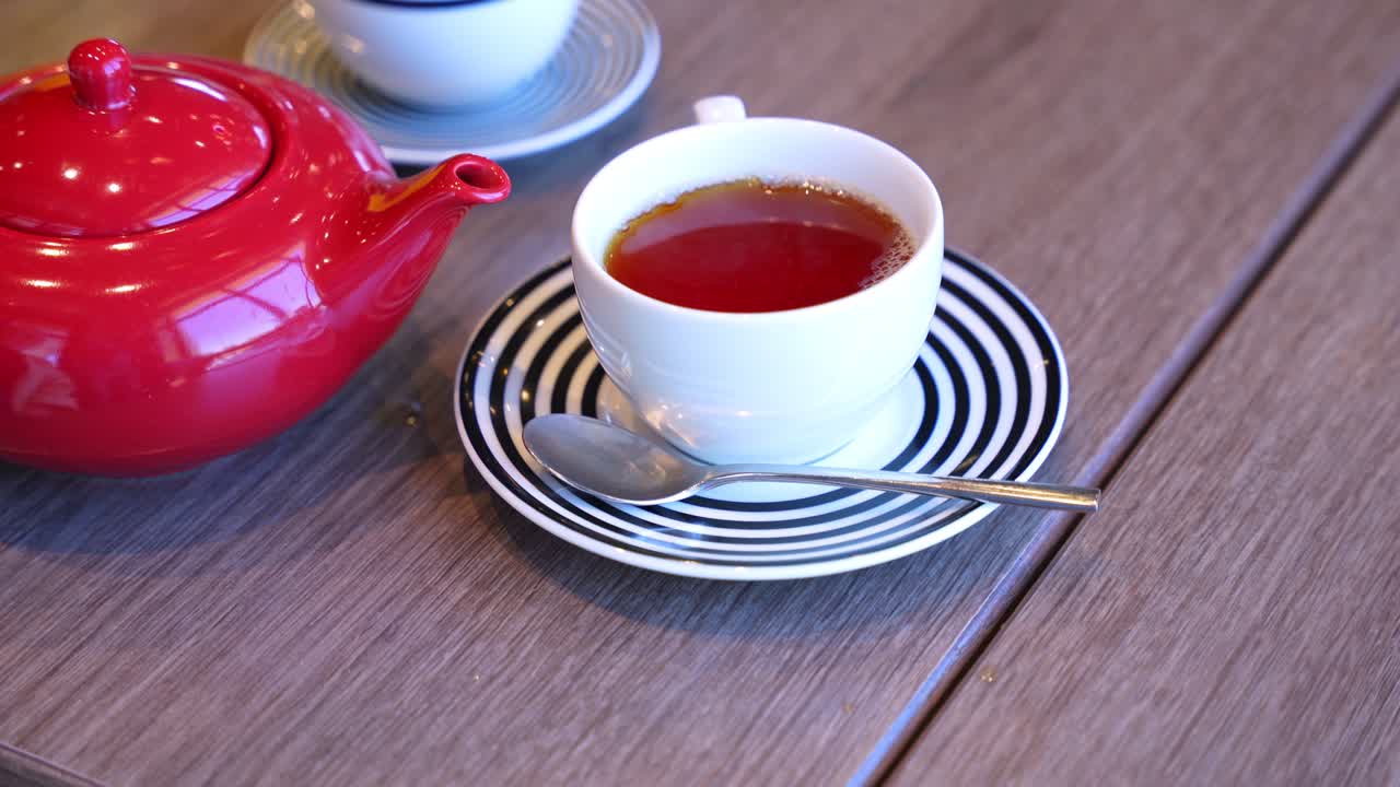 Top-down shot of black tea in white cup beside red teapot. Ideal for café, lifestyle, or morning beverage visuals