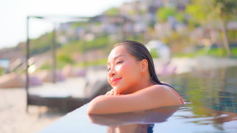 Close-up-of-a-young,-attractive-woman-in-a-swimming-pool-rests-her-head-on-her-arms-as-she-closes-her-eyes-to-daydream