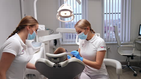 young beautiful female dentist taking a metal instrument. doctor is starting dental examination of a little boy. nurse sitting on the other side of a patient.