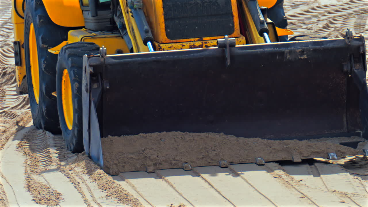 Close up of an yellow wheel loader moving on the sandy beach