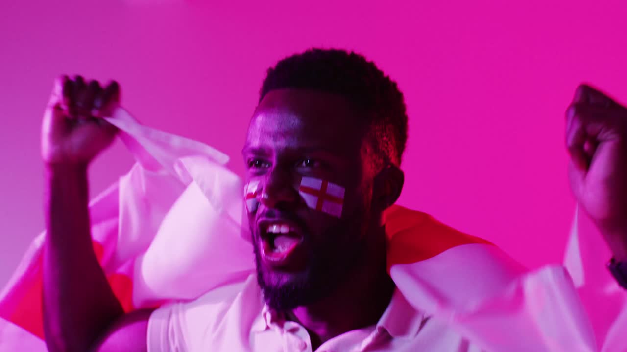 Video of joyful african american male sport fan with flag of england on neon pink lightning