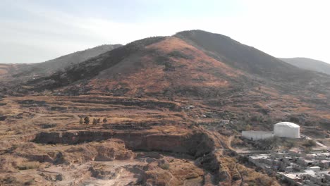 Vista-Aérea-De-4k-De-La-Cordillera-Al-Lado-Del-Campo-Desnudo-Excavado-En-El-Suelo-Y-El-área-Residencial