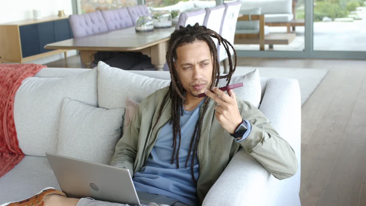 Man in thirties at home with laptop grabbing vibrating phone, switching to speaker, answering call
