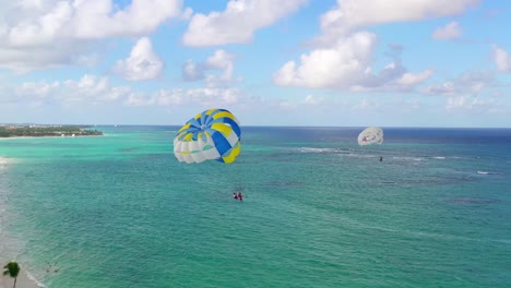 vista escénica de dos personas haciendo parasailing juntas en paracaídas amarillo y azul por la playa de arena punta cana resort, república dominicana, antena