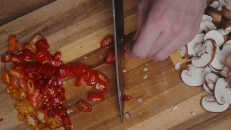 Red-chilis-being-cut-on-a-wooden-board-by-professional-chef-in-an-elegant-black-shirt-with-tattoos